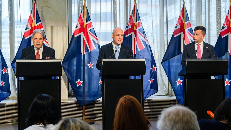 Novi premijer Novog Zelanda Kris Lukson (u sredini) sa koalicionim partnerima Vinstonom Petersonom (levo), liderom stranke „Novi Zeland na prvom mestu", i Dejvidom Simurom (desno), liderom stranke „Deluj"