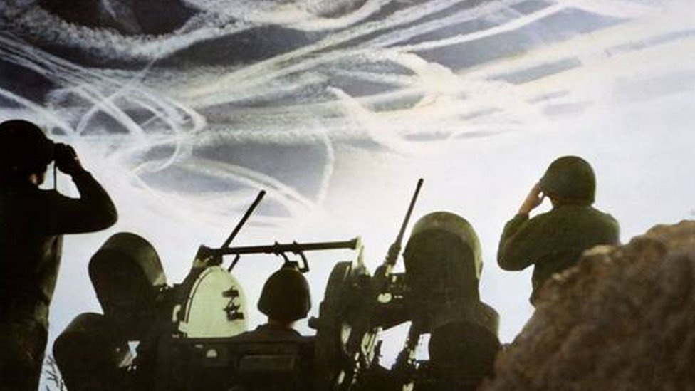 Soldados olham para o céu cheio de rastros de avião