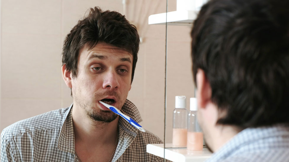 Hombre con resaca o gripe mirándose en el espejo.
