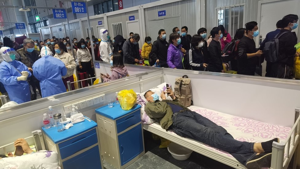 Um homem em uma cama de hospital com uma longa fila de pessoas na fila para deixar o hospital