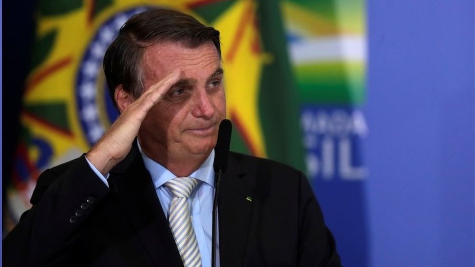 Jair Bolsonaro faz continência diante da bandeira do Brasil