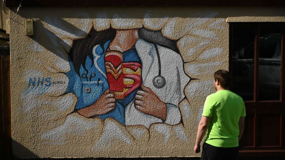 Мужчина смотрит на уличное искусство супергероев NHS