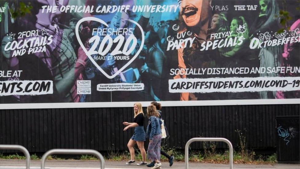 Молодые женщины идут рядом с плакатом университета