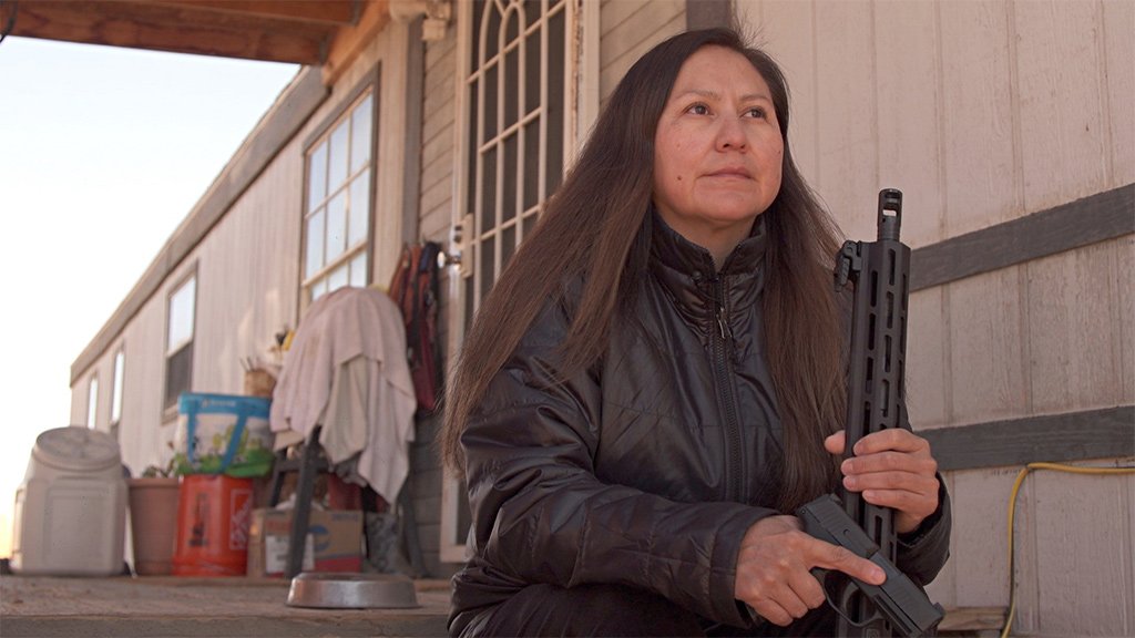 Shiprock resident Bea Redfeather sits on her porch holding guns she bought to protect her family