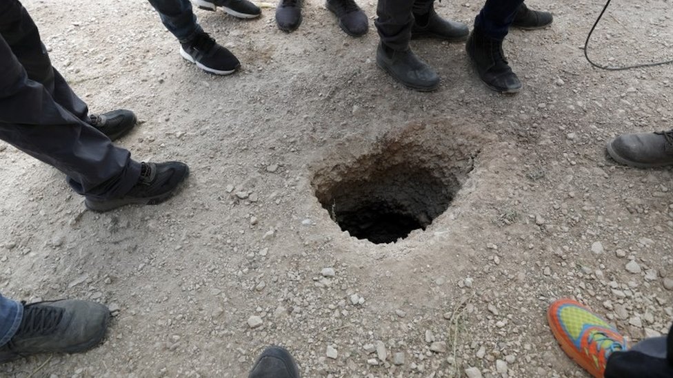 Police officers and journalists gather around the exit of a tunnel allegedly used to escape from Gilboa Prison, northern Israel (6 September 2021)