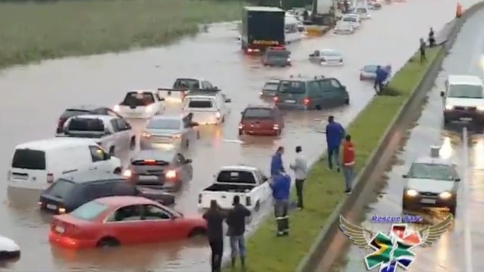 Люди, стоящие в центральной резервации, смотрят на затопленные автомобили на затопленной дороге во время шторма в Дурбане, Южная Африка, 10 октября 2017 г.