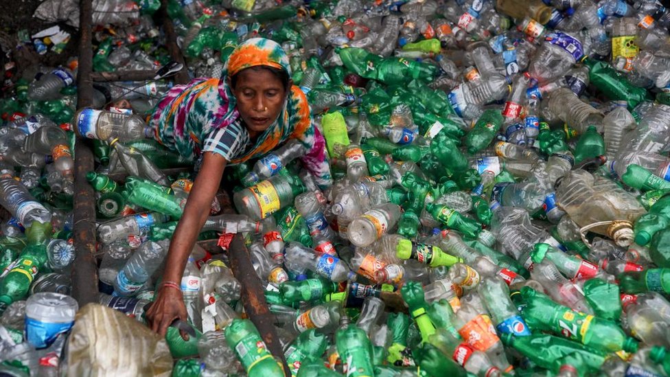 Una mujer en medio de botellas de plástico para reciclar.