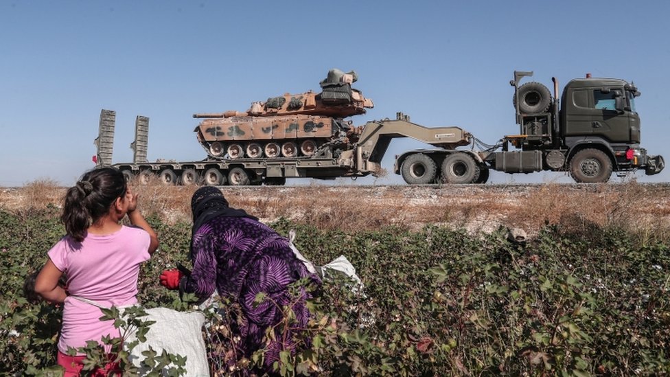 Seasonal workers cut a cotton while Turkish military vehicles carrying tanks as they are on the way to Northern Syria for a military operation in Kurdish areas, near the Syrian border, near Akcakale district in Sanliurfa, Turkey 12 October 2019.