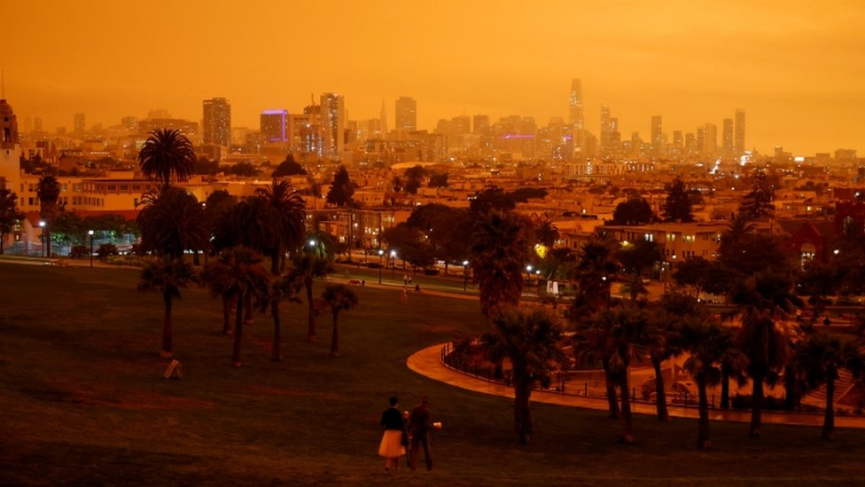Downtown San Francisco is seen from Dolores Park under an orange sky