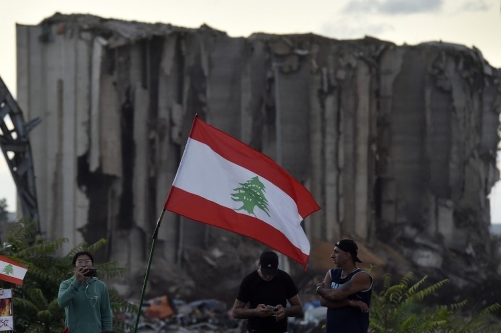 أشخاص يحملون الأعلام اللبنانية وهم يتجمعون لإحياء الذكرى الثانية لبداية الحركة الاحتجاجية المناهضة للحكومة ، أمام صوامع الحبوب المدمرة في مرفأ بيروت (17 أكتوبر / تشرين الأول 2021)