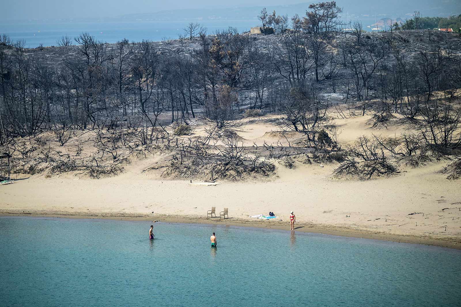 ​​A woman enters the sea from a beach where wildfires destroyed the woods, near the village of Gennadi in the southern part of the Greek island of Rhodes - 27 July 2023