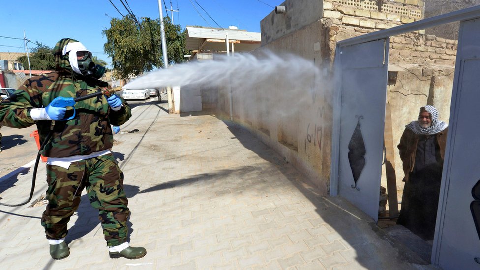 Иракский мужчина выглядывает из дверного проема, когда работник гражданской обороны дезинфицирует район Наджафа, где были обнаружены случаи заболевания Covid-19 (3 ??февраля 2020 г.)