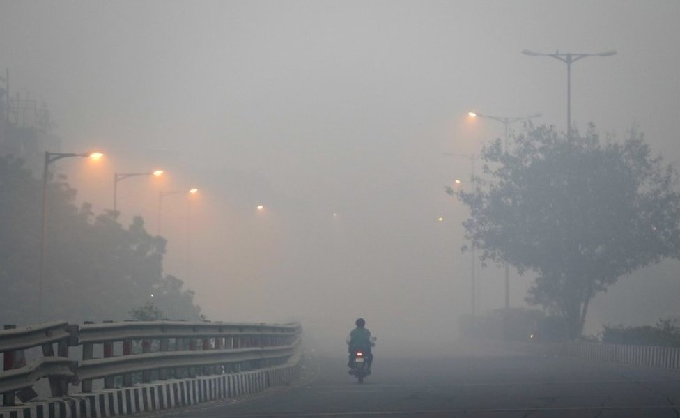 Мужчина едет на скутере по дороге, окутанной дымом и смогом, утром после фестиваля Дивали в Нью-Дели, Индия, в понедельник, 31 октября 2016 г.
