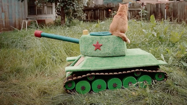 Picture of a cat sitting on a tank-shaped pet house.
