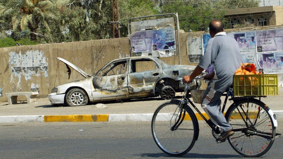 An Iraqi man rides a bicycle past the remains of a car burnt during a deadly incident involving Blackwater guards in Baghdad in September 2007