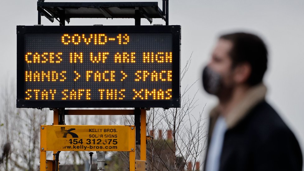 A man walks past a sign warning of high Covid cases