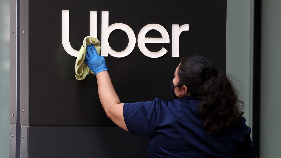 Mujer limpia el logo de Uber en su sede en San Francisco, California.