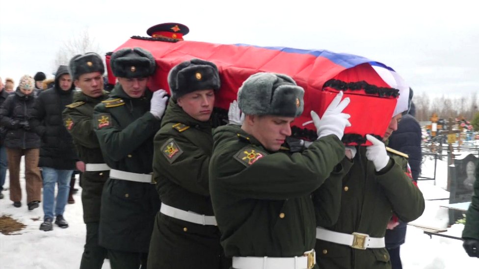 Russian servicemen carry a coffin draped in the national flag through a snowy cemetery