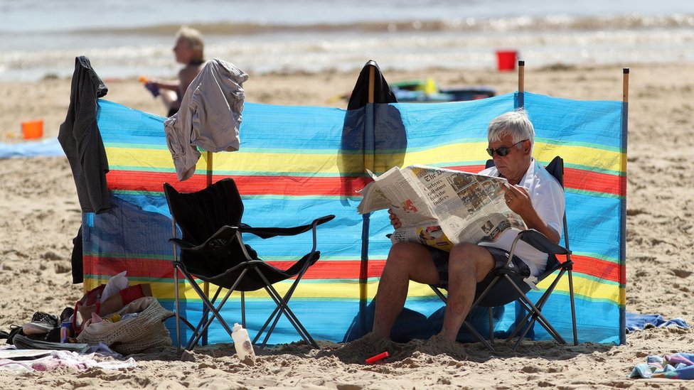 Мужчина читает газету на пляже в Великобритании