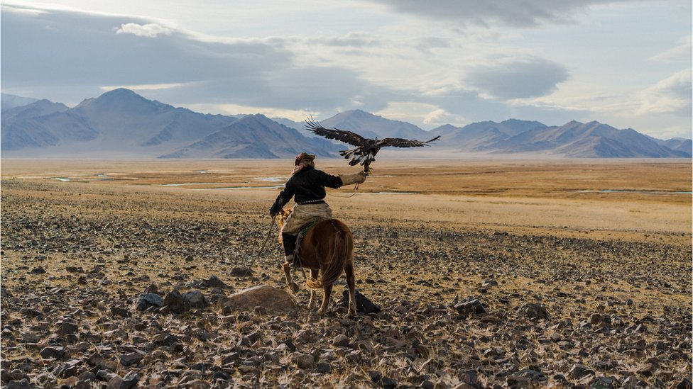 Un hombre montado a caballo sujeta un águila en la estepa mongola.