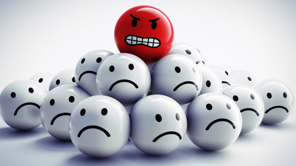 Un emoji rojo con expresión de enfado encima de un grupo de emojis blancos con expresión de tristeza