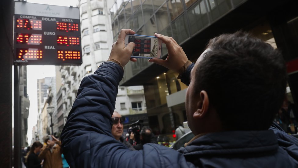 A man takes picture of a screen showing exchange rates in Buenos Aires