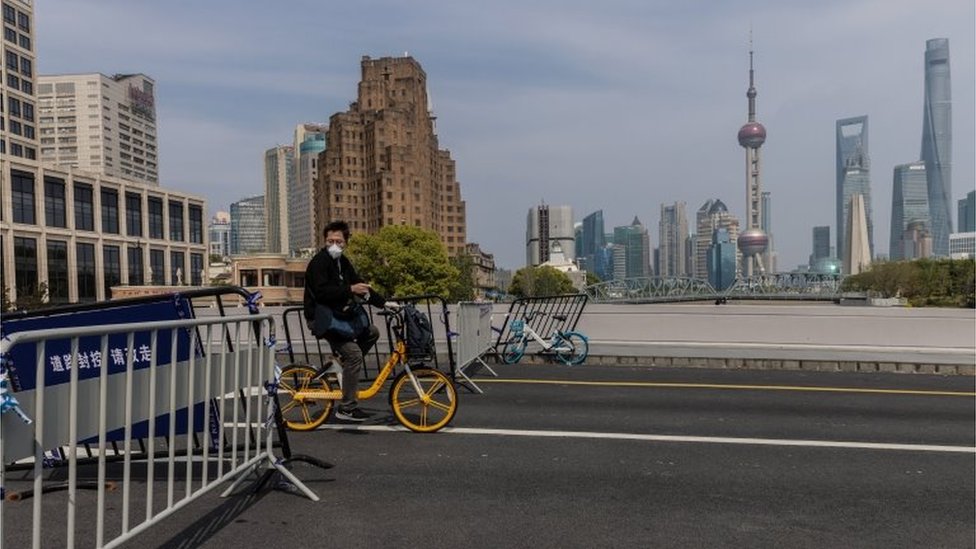 一名男子在上海騎著自行車穿過橋上的疫情封鎖路障
