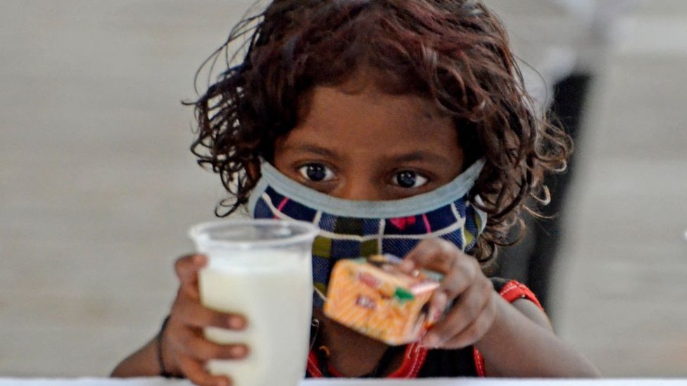 Un niño toma un vaso de leche y un paquete de galletas durante la distribución gratuita organizada por la policía de Kolkata en medio de una emergencia por el coronavirus en Kolkata, India, el 23 de mayo de 2021.