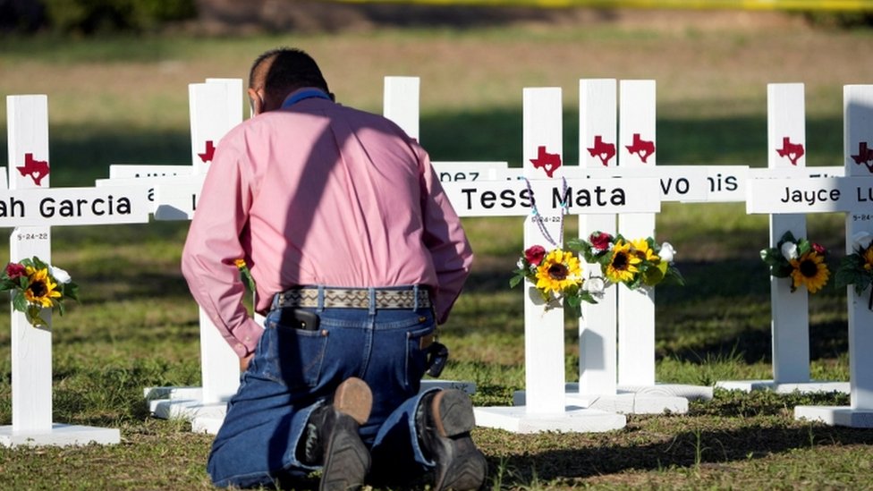Un hombre arrodillado frente a varias cruces en honor a las víctimas del tiroteo.