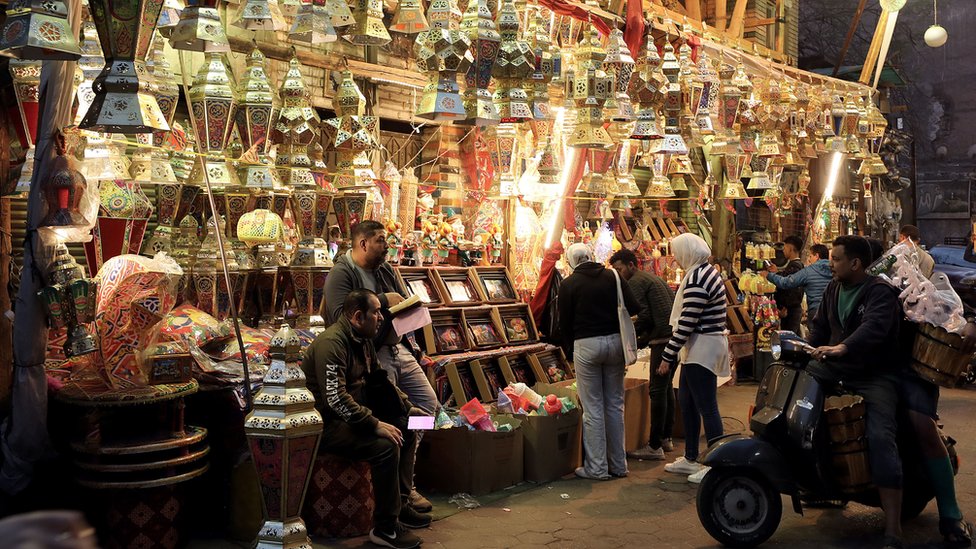 سوق وفوانيس رمضان وأشخاص تتجول في السوق.