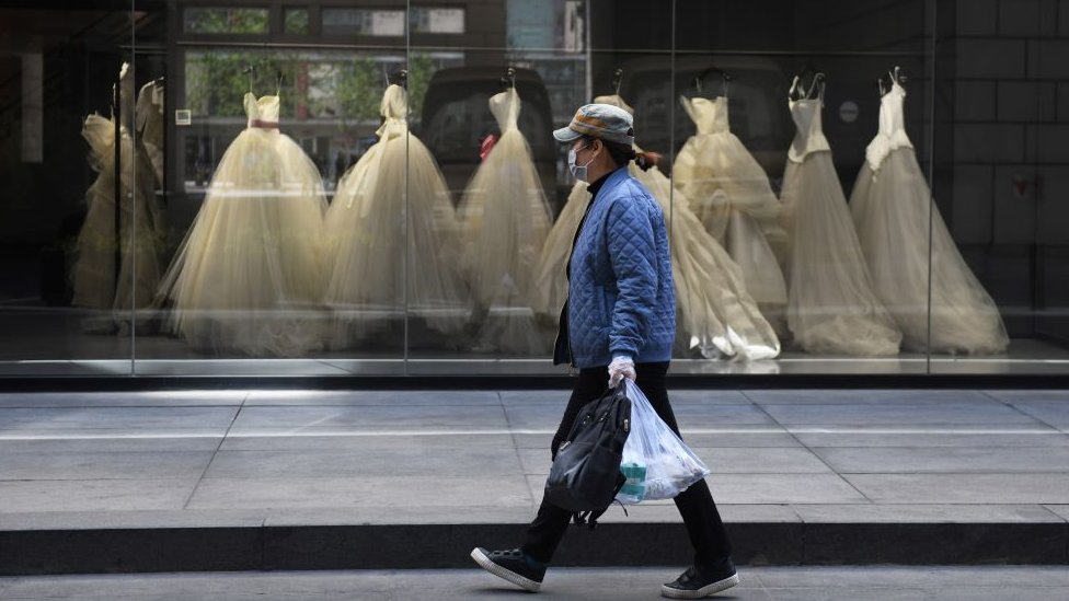 A woman walks past wedding dresses displayed in a Vera Wang bridal store in Beijing on April 22, 2020.