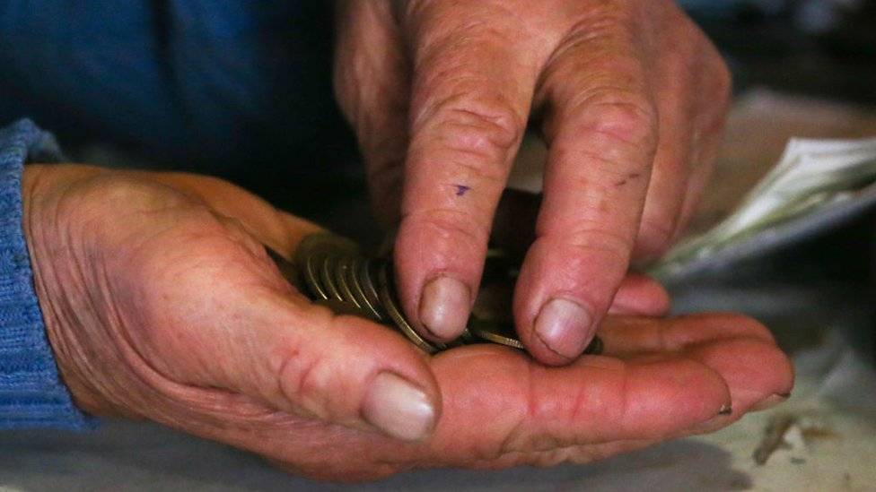 Manos de un hombre mayor contando monedas.