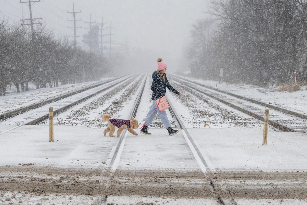 A woman walking her dog crosses train tracks as heavy snowfall begins in a western suburb of Chicago, 22 December 2022