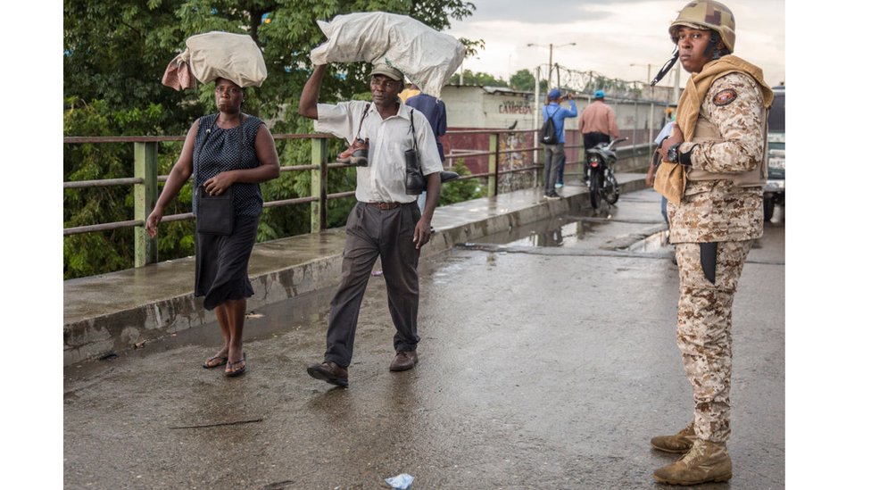 Oficial de la frontera, en puente, dos personas cruzan puente