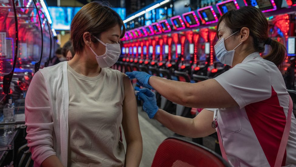Mulher sendo vacinada por profissional da saúde dentro de um pachinko