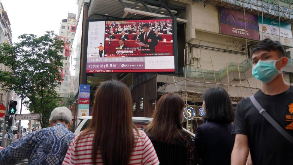 Menschen mit Gesichtsmasken gehen in Hongkong an einem großen Bildschirm vorbei und zeigen eine Live-Übertragung auf der Straße des Nationalkongresses