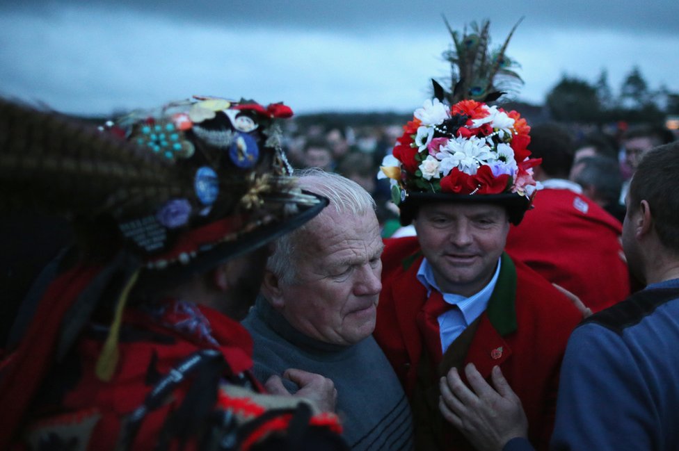 Дурак Хэкси, Дейл Смит (слева, лицо не видно) и вождь Боггин Фил Палмер (справа) и жители деревни готовятся начать игру «Хакси Гуд»