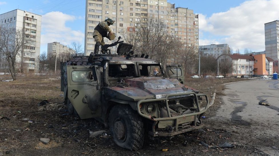 A Ukrainian territorial defence soldier examines a burnt-out Russian army vehicle in Kharkiv