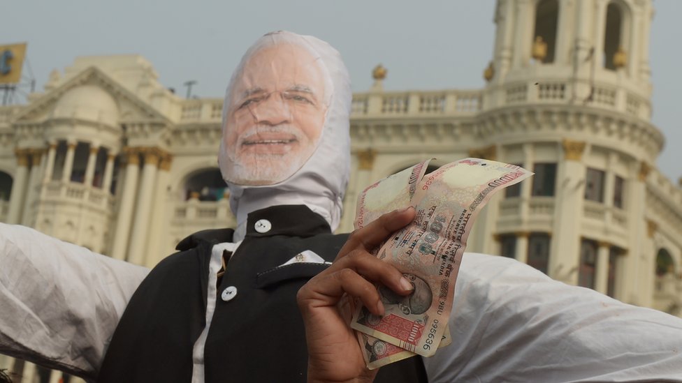 Мужчина держит банкноты в 1000 рупий на подставке Моди