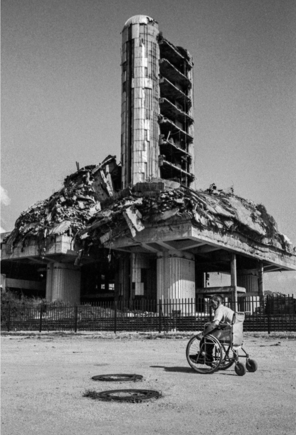 Вид на разрушенное войной здание с человеком в инвалидной коляске перед ним