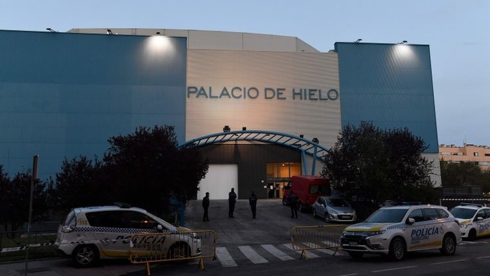 Полицейские стоят у торгового центра Palacio de Hielo (Ледяной дворец), где 23 марта 2020 года ледовый каток был превращен во временный морг в Мадриде, чтобы справиться с ростом смертности в испанской столице из-за коронавируса