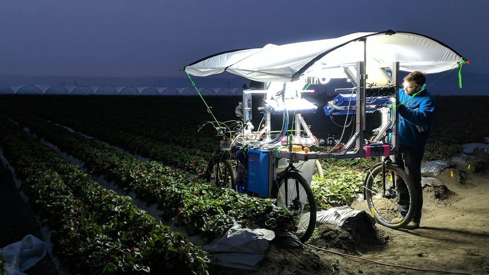 A man works on a prototype buggy in a field at night - this version looking like a large table mounted on bicycle wheels, with computer kit on the flat surface