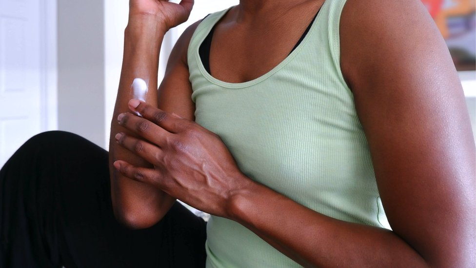 Close-up of unrecognizable black woman rubbing lotion into arm
