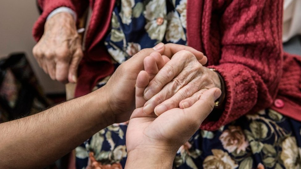 Cuidador sosteniendo las manos de una persona mayor