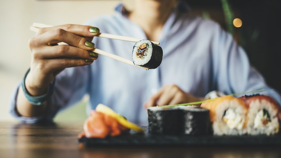 Mujer comiendo sushi.