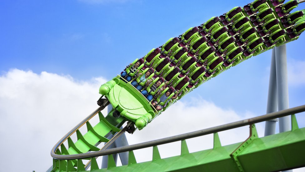 Personas sentadas en la primera fila de la montaña rusa verde mientras gira en una curva