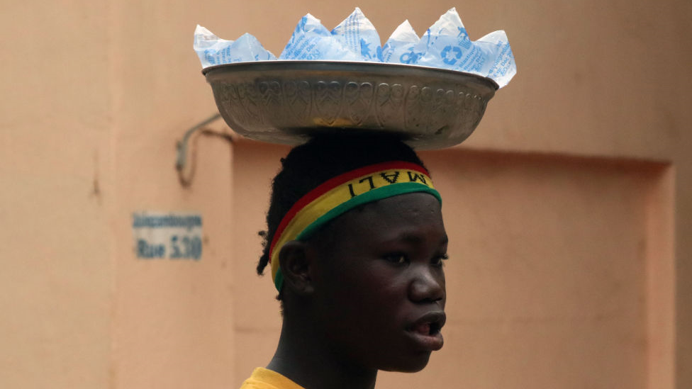 A young man is seen with cold water bottles on his head in hot weather reaching 40 degrees in Bamako