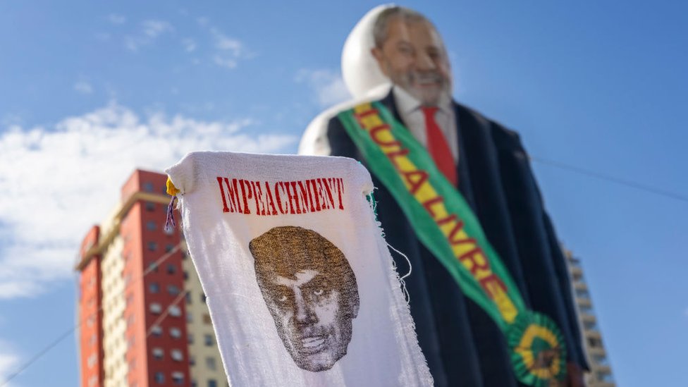 Cartaz em tecido diz Impeachment, sobre uma imagem de Jair Bolsonaro, com um boneco de Lula usando uma faixa presidencial escrita 'Lula Livre' ao fundo