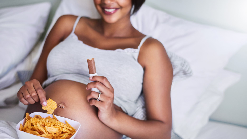Black pregnant woman eating chocolate and potato chips
