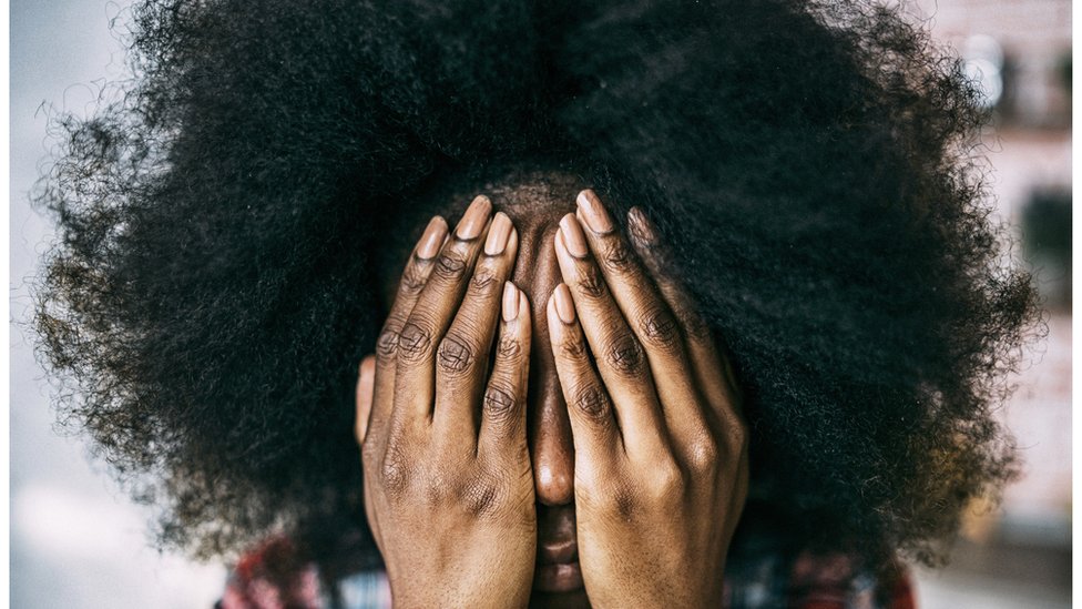Черная женщина закрывает лицо руками